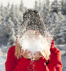 Young woman blowing snow from hands in a sunny day in the countryside