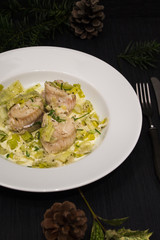 Rolls of cod in leek-cream sauce. White plate and black ground.