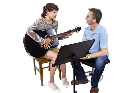 Music teacher tutoring young female student how to play guitar