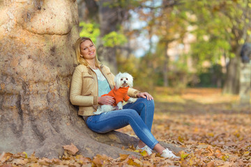 Fototapeta premium Young woman enjoying nice autumn day in a park with her cute little Maltese dog