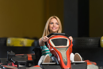 Fototapeta na wymiar Young Woman Is Driving Go-Kart Car With Speed In A Playground Racing Track - Go Kart Is A Popular Leisure Motor Sports
