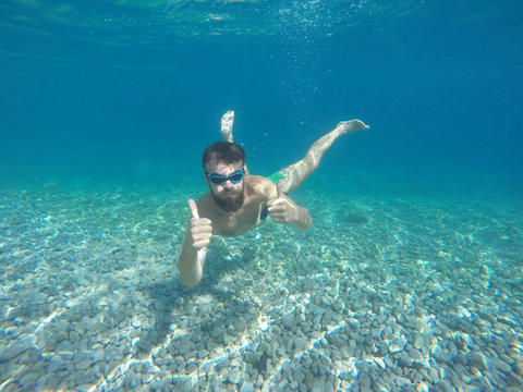 Young beard man with mask diving in a clean water