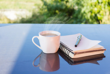 Classic white cup of black coffee decorated with note and pen with green nature background