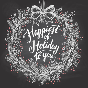 Happiest of holiday to you. Calligraphy quote with Christmas wreath on blackboard with chalk