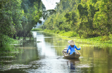 Fototapeta na wymiar Woman rowing on the river and passed the house homeland with small body, shirt Ba Ba and conical hats typical of Southeast women in a spring afternoon in Dong Thap, Vietnam