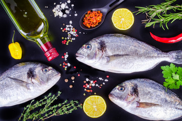 Fresh raw gilthead fishes with lemon, herbs, salt on black background. Healthy food concept. Food frame