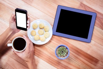 Overhead of feminine hands holding smartphone and coffee