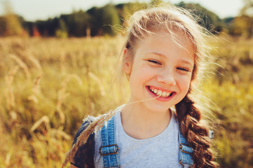 happy child girl in jeans overall playing on sunny field