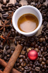 Obraz na płótnie Canvas cup of coffee with coffee beans, cinnamon, star anise and red christmas ball on wood
