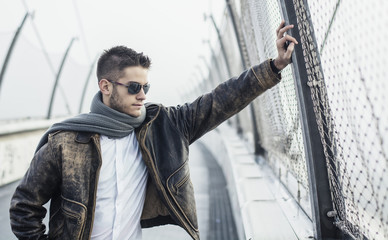 Handsome trendy man standing on a bridge, looking down