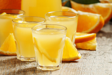 Orange juice with fruit pieces in small cups and a jug on old wo