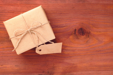Obraz na płótnie Canvas Gift box into brown paper tied by twine with blank tag on old wooden table with space for text