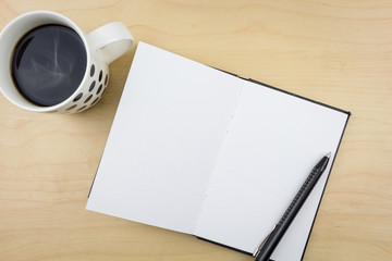 Open notebook with black pen and a cup of coffee, on wooden surface.