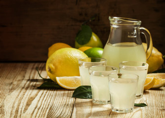 Home lemon liqueur and fresh lemons and limes on a wooden backgr