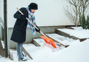 Mid adult woman in black jacket, removing snow in front of her hous