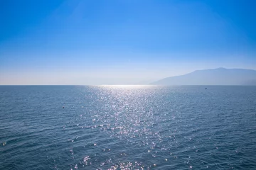 Photo sur Plexiglas Côte Paysage marin avec ciel bleu et eaux, avec des terres lointaines cachées dans la brume.