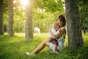 Naklejka na ściany i meble Mom and son sitting in a meadow on a sunny summer day, the boy hiding in his mother's bosom.