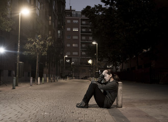 young sad woman sitting on street ground at night alone desperate