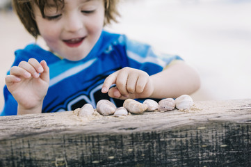 A boy at the beach counting shells lined up on a breakwater. 