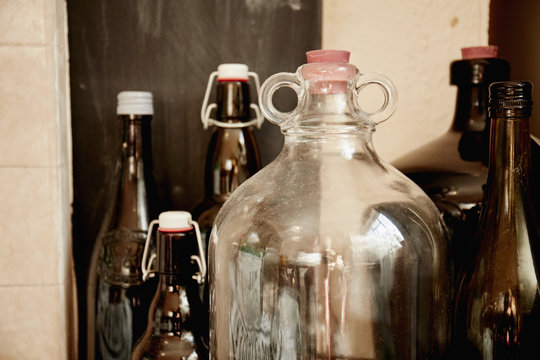A shelf of bottles and jars, one large double handled jar with a stopper and bottles with lids. 