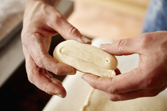 A baker holding dough which has been folded and worked to show the layers incorporated into the dough, to make light layered pastries. 