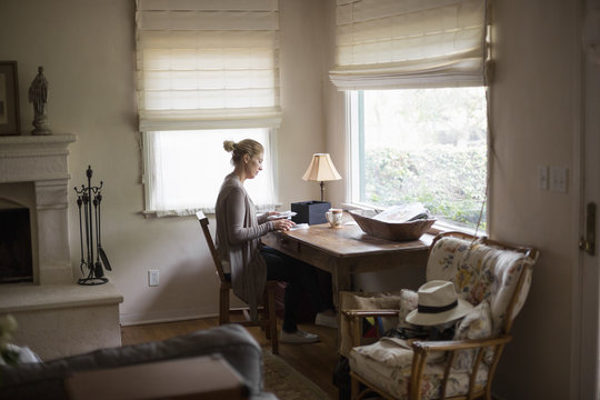 Blond woman sitting at a desk by a window, looking at photographs.