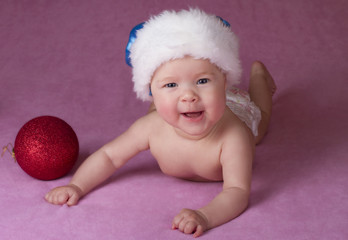 Joyful little baby in Christmas hat and Christmas decoration on a pink background 