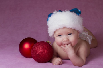 Joyful little baby in Christmas hat and Christmas decoration on a pink background 