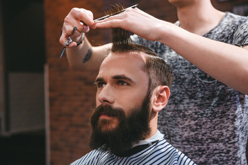 Handsome bearded man having haircut with comb and scissors