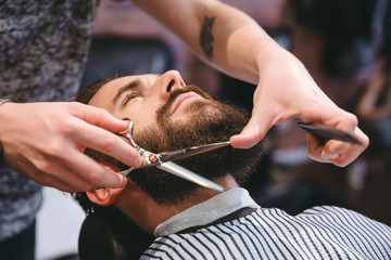 Fototapeta Hairdresser doing haircut of beard to young attractive man obraz