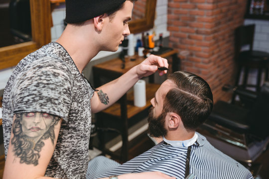 Young hairstylist combing hair of male client with comb