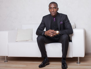 Studio fashion portrait of a handsome young African American businessman wearing a black suit and tie.