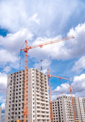 Fototapeta na wymiar Multistorey houses under construction and industrial cranes