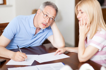Fototapeta premium Senior couple working out their bills at home in the kitchen