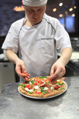 chef baker in white uniform making pizza at kitchen.Focus on the pizza