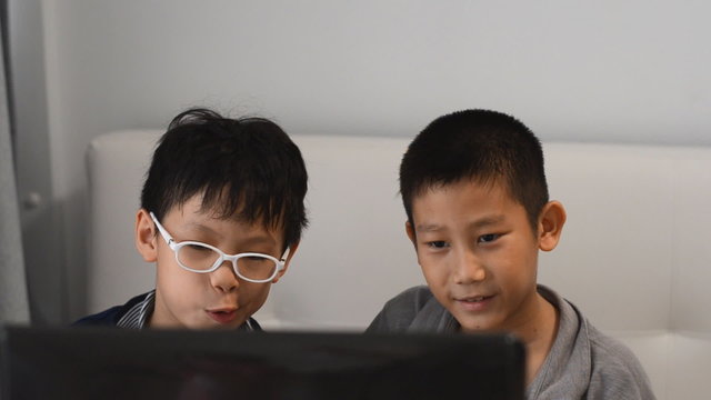 Young Asian children playing game on laptop computer
