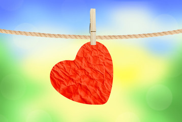 Crumpled paper heart hanging on rope over nature background