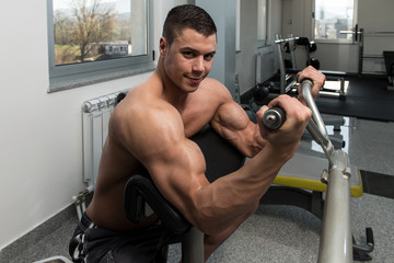 Fototapeta na wymiar Man In The Gym Exercising Biceps On Machine