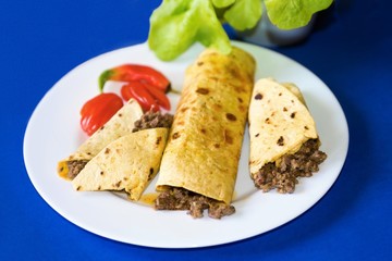 Tortilla with minced beef on blue background with green salad