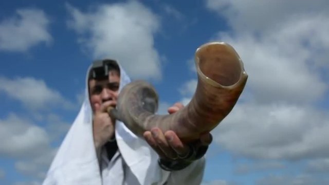 Jewish man blow Shofar (Horn) outdoors under the sky, on the Jewish High Holidays in Rosh Hashanah and Yom Kippur