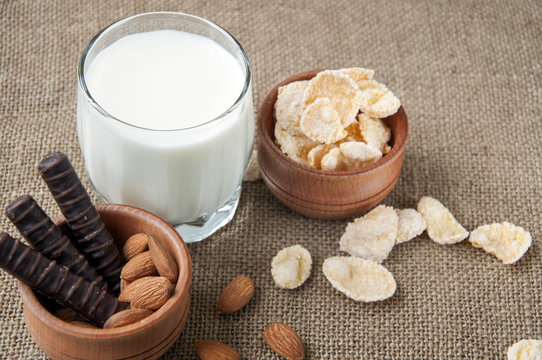 A glass of milk with almond nuts, corn flakes, chocolates,  on sacking, burlap background