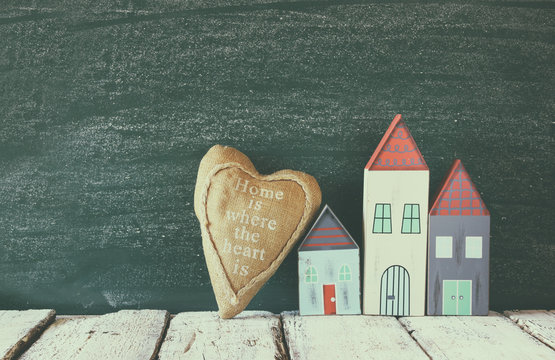 image of vintage wooden colorful houses and fabric heart on wooden table in front of blackboard
