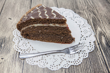 Fresh tasty sweet piece of  chocolate cake on a white napkin and a dessert fork on a wooden background