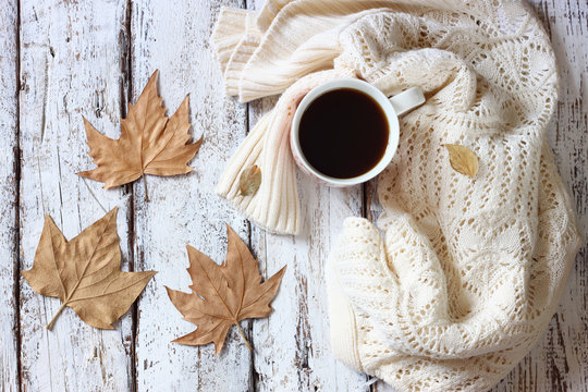 top view image of white cozy knitted sweater with to cup of coffee and autumn leaves on a wooden table