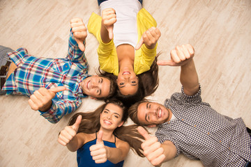 Cheerful young people lying on the floor showing thumbs up