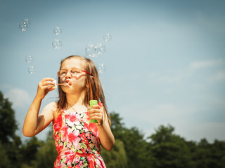 Little girl having fun blowing soap bubbles in park.