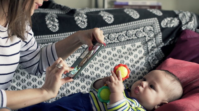 Young mother taking photo of her child with toy on sofa at home
