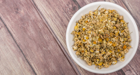 Dried chamomile herbal tea in white bowl over wooden background