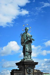 Fototapeta na wymiar statue of John of Nepomuk in Prague on the Charles Bridge on the background of blue sky with clouds. Czech Catholic saint, priest, martyr