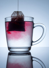 tea bag in a transparent mug with beautiful abstract stains in water with reflection on a grey background
